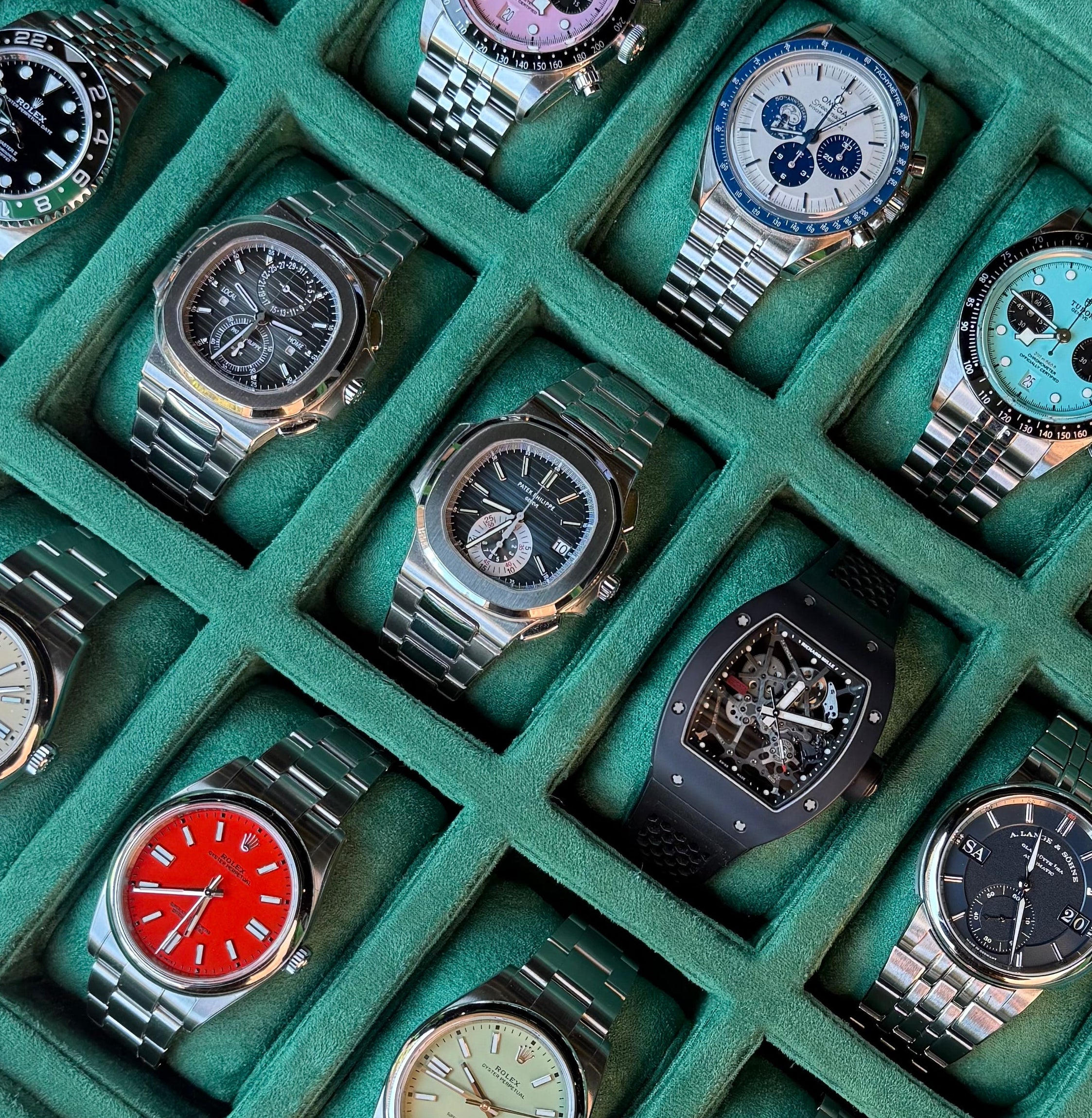 Collection of luxury watches in a green display case on a dark surface